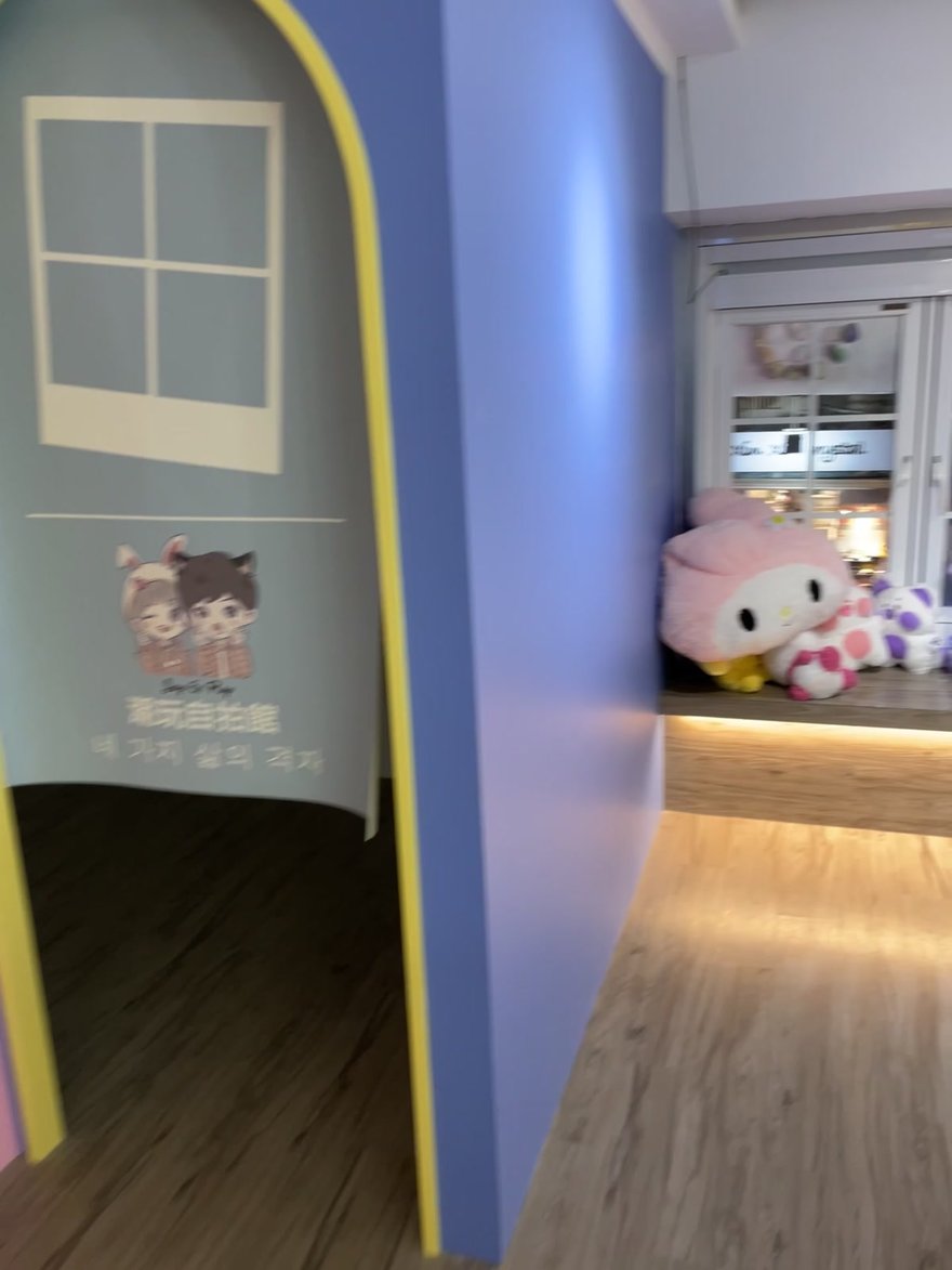 Joy&Ray 西門店的拱形棚門，門面漆成粉藍與鵝黃，拱門上印 Joy & Ray 卡通人物與潮玩自拍館字樣，旁邊窗台放著三麗鷗絨毛娃娃