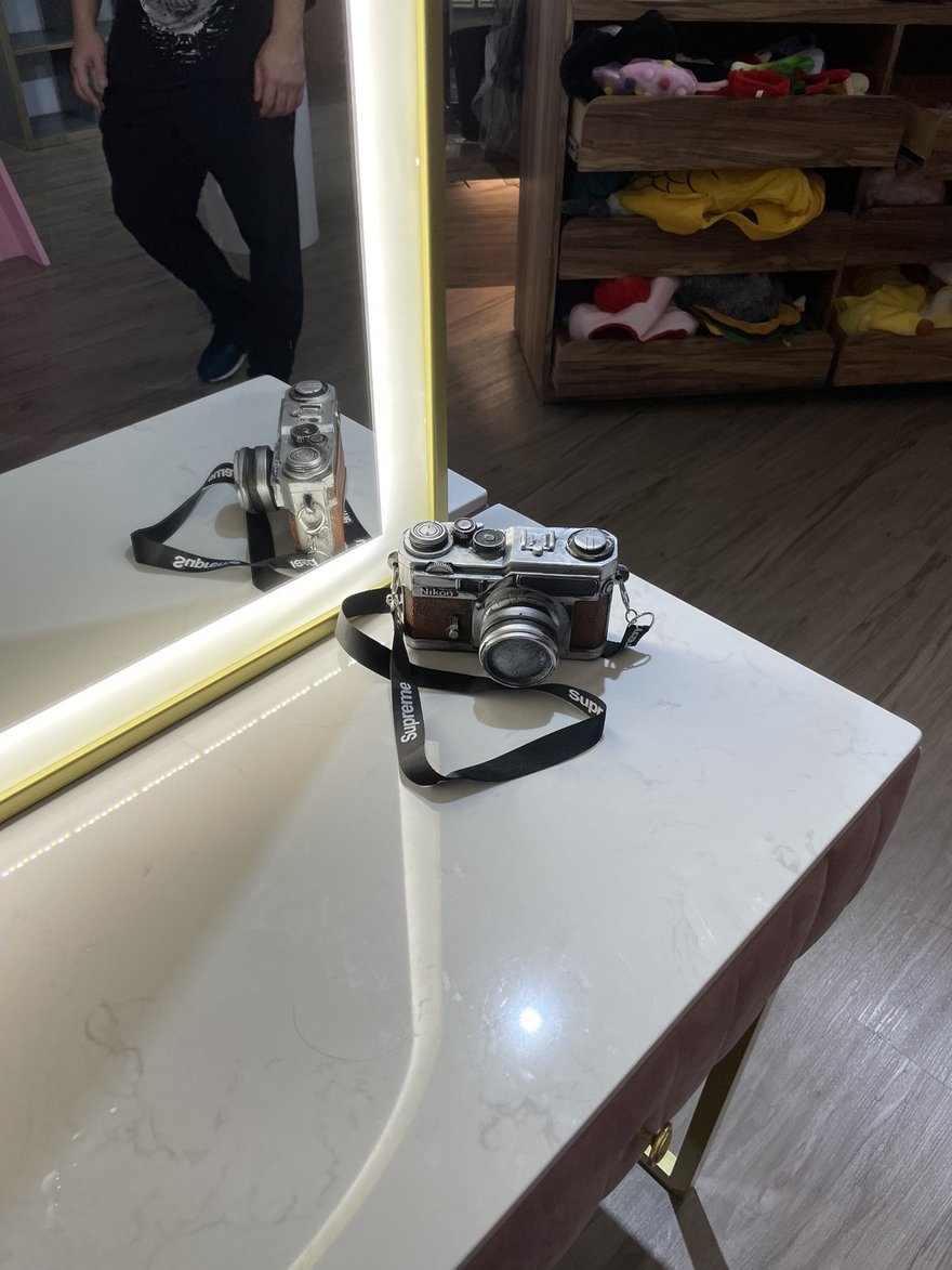 Joy&Ray 西門店的化妝檯與造型道具，大理石檯面配金框環狀燈鏡，檯面上擺 Nikon 復古底片相機造型道具並掛 Supreme 背帶