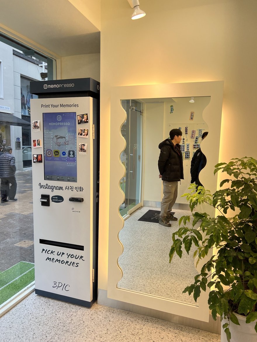3PIC 門口的 memopresso 印相機，白色機身面板寫 memoPresso、Print Your Memories 與 Instagram 사진 인화，下方印 PICK UP YOUR MEMORIES 與 3PIC