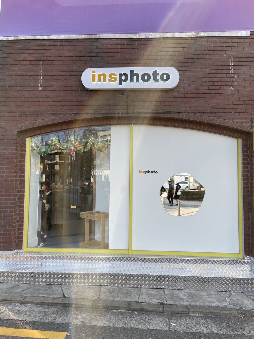 insphoto 的店面外觀，紅磚立面搭配黃色窗框，招牌以白底圓角膠囊造型寫 insphoto，櫥窗上嵌有圓形鏡面