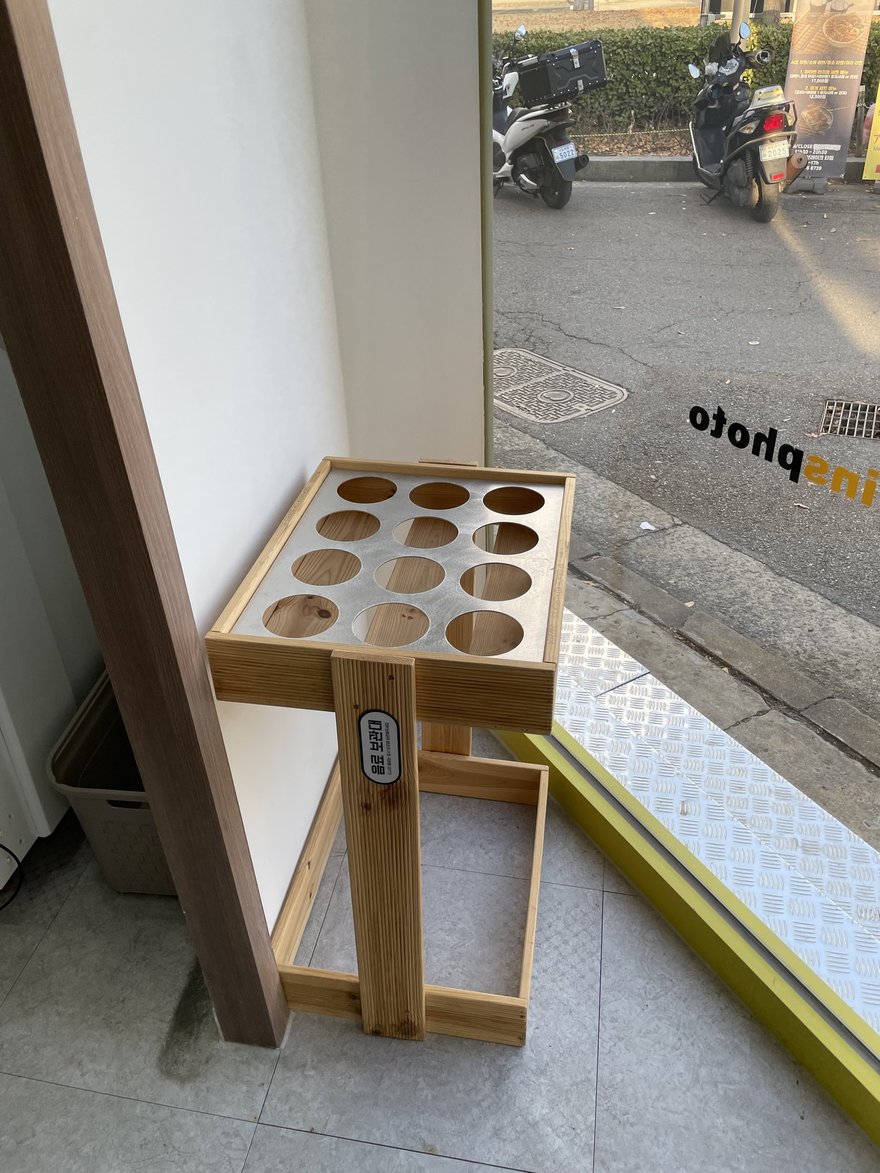 insphoto 門口人行道上的木製道具架，檯面挖出十二個圓孔用來插放拍攝小物，架子擺在店門外的人行道上