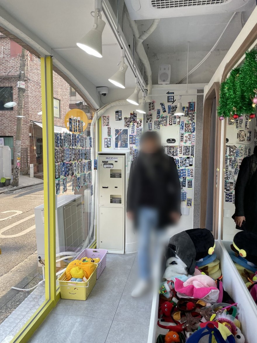 insphoto 店內的狹長空間，右側牆面貼滿顧客樣張，左側為落地窗，門口地上放著一籃橘子與成堆道具
