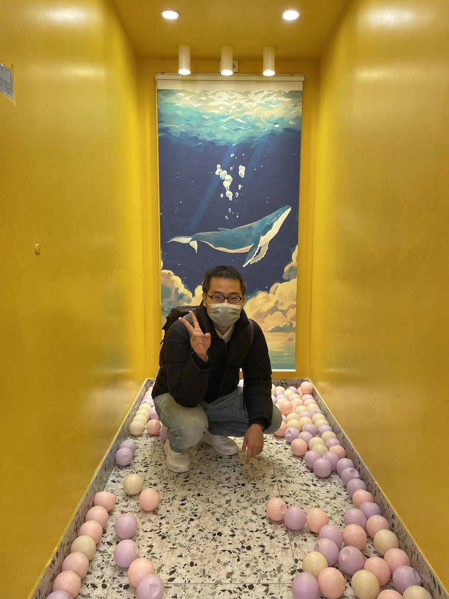 인생네컷店內的黃色球池走廊，地面鋪滿粉色球池、盡頭牆面為藍色鯨魚插畫