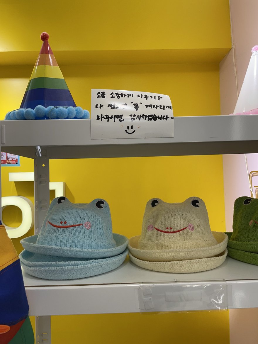 인생네컷店內的蛙型玩偶道具層架，黃色牆面搭配彩色帽子道具