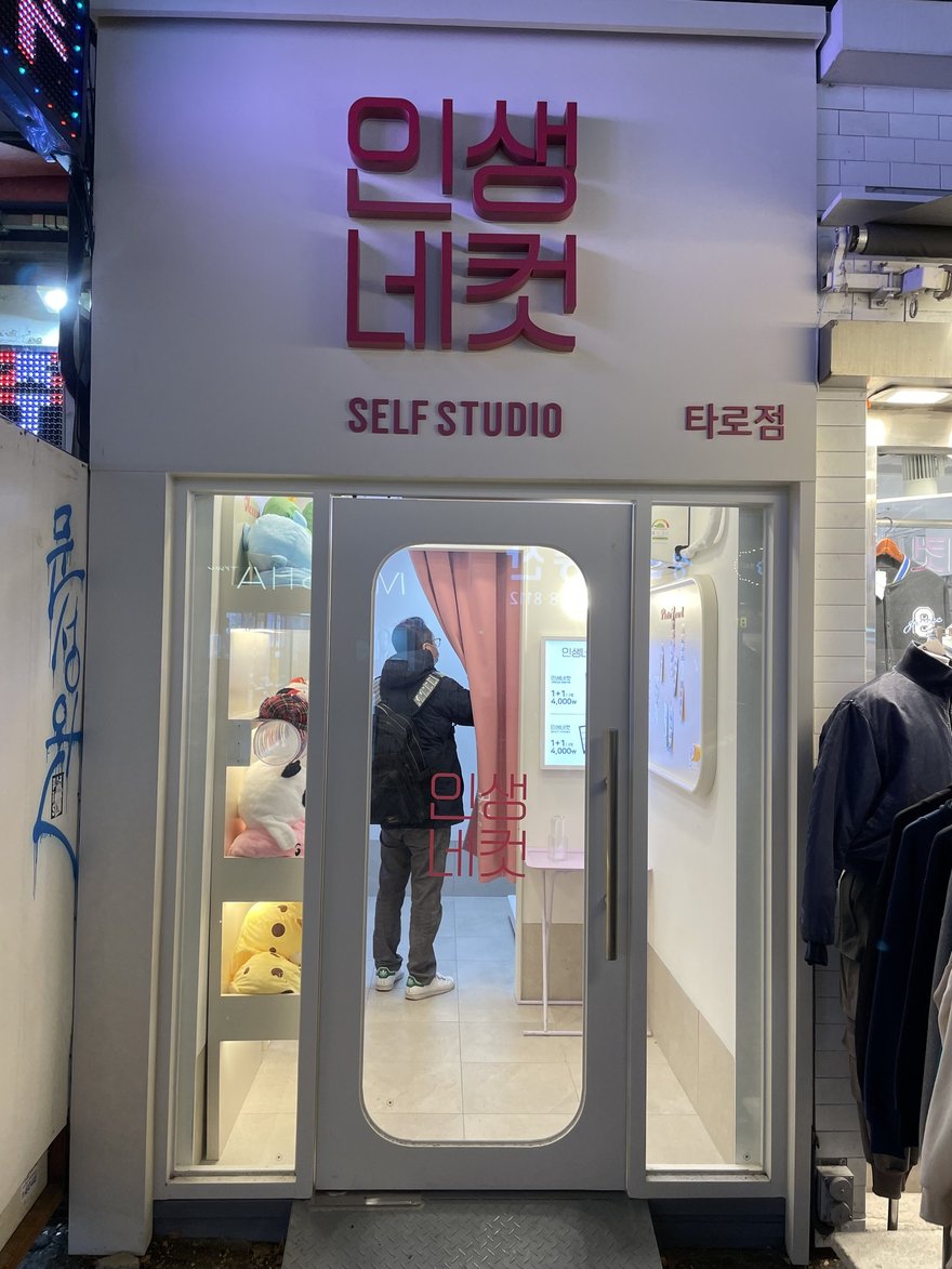 인생네컷門市的夜間外觀，招牌下方另掛塔羅점標示，門口有顧客進出