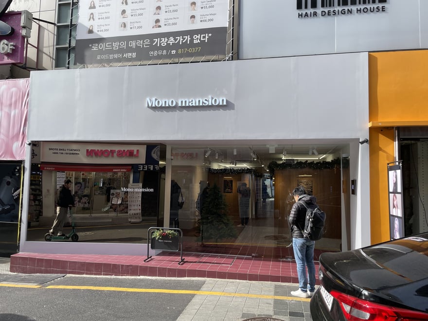 釜山西面 Mono mansion 的店面街景，白色招牌以襯線字體寫 Mono mansion，同一棟樓的鄰店招牌可見로이드밤헤어 서면점與 051 開頭的電話號碼
