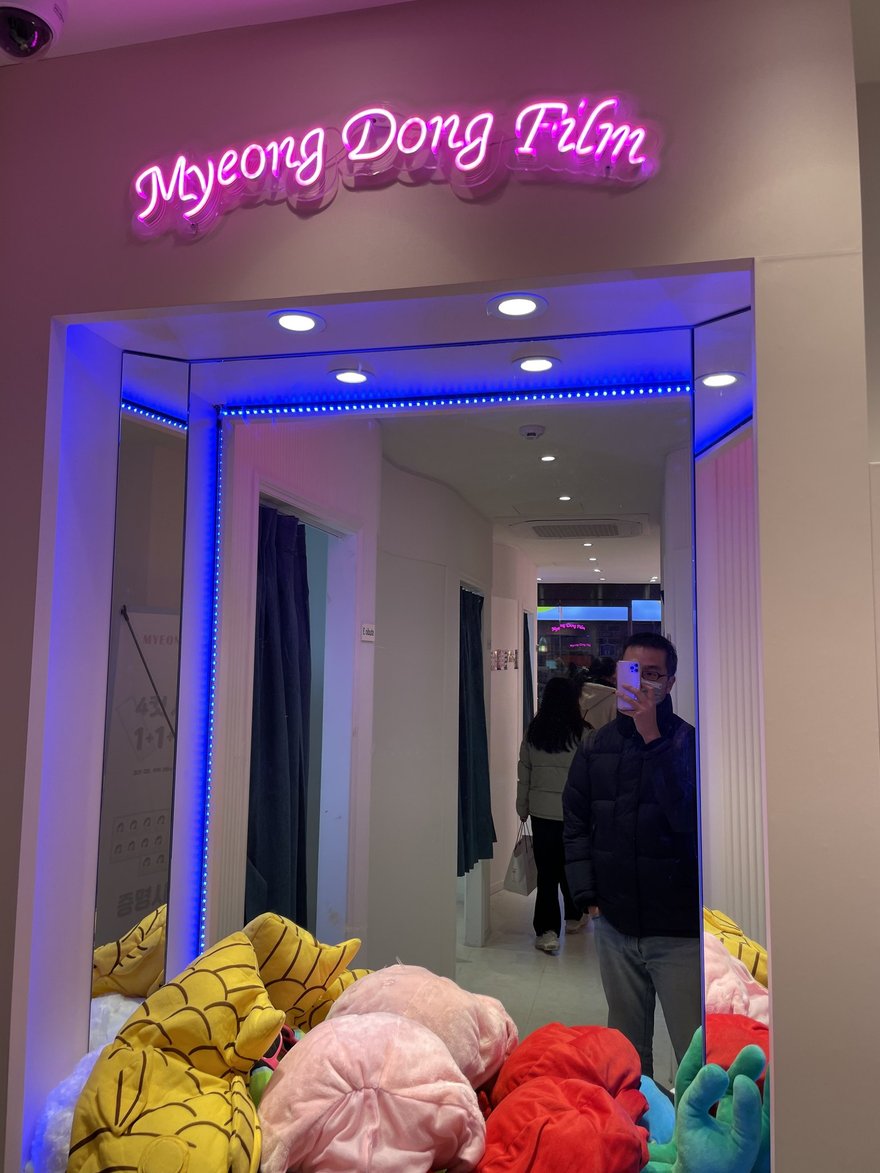 Myeong Dong Film 店內入口的藍色燈框走道，前方地面堆放黃色與粉色的大型絨毛玩偶