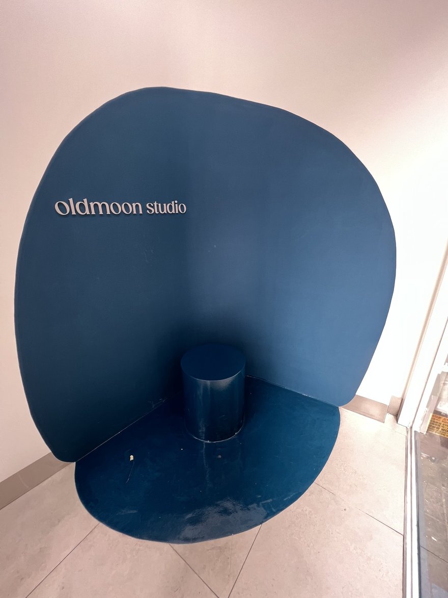 印有 oldmoon studio 字樣的深藍色圓形拍攝背板，拍攝於店招為 Mono mansion 的門市內