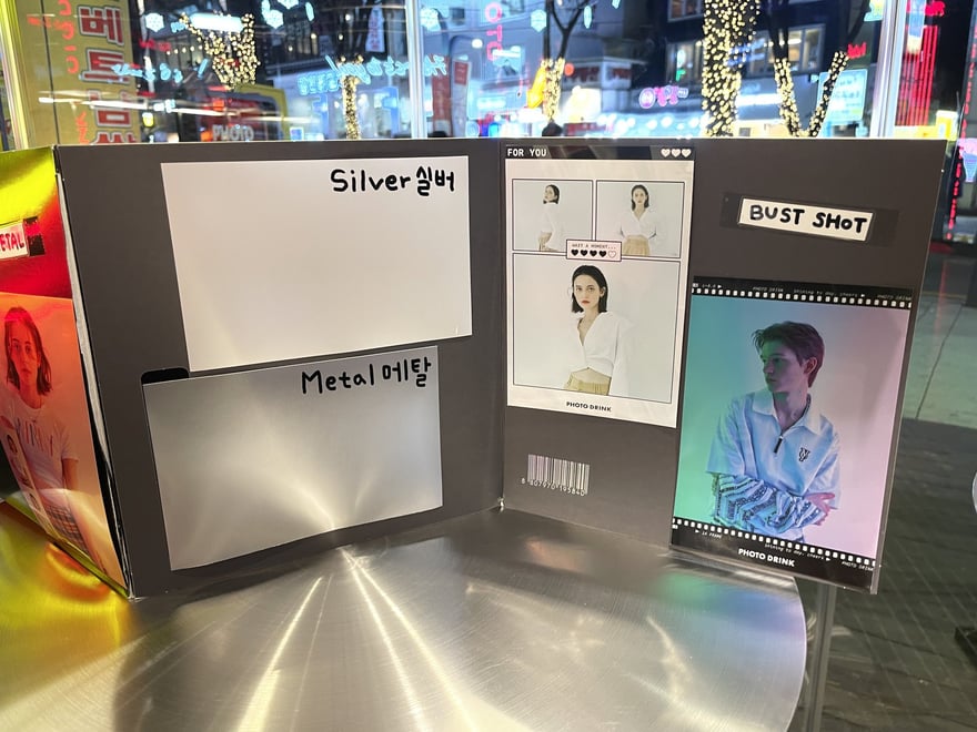 PHOTO DRINK 的樣張展示架，以 Silver 실버、Metal 메탈與 BUST SHOT 等名稱標示不同相紙材質與版型