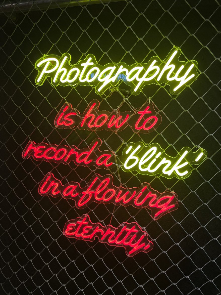 PHOTO DRINK 店內的 Photography is how to record a blink in a flowing eternity 霓虹標語，黃色手寫字體