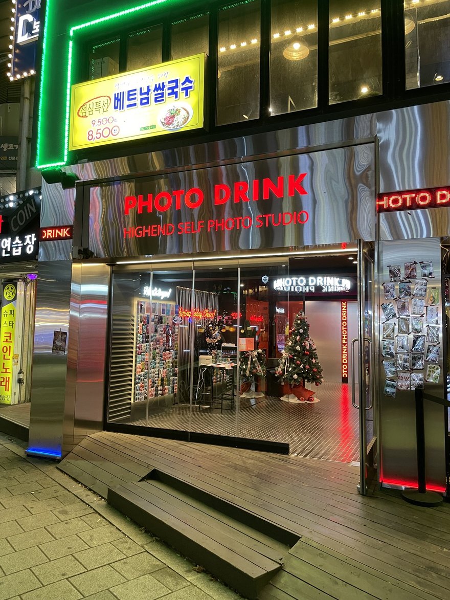 PHOTO DRINK 第二家門市的夜間外觀，招牌燈亮著，門口為階梯與街道