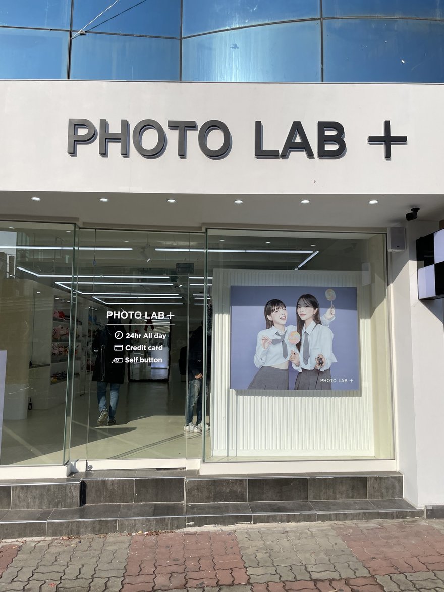 PHOTO LAB+ 門市的玻璃立面與騎樓入口，玻璃上印品牌名與模特兒燈箱