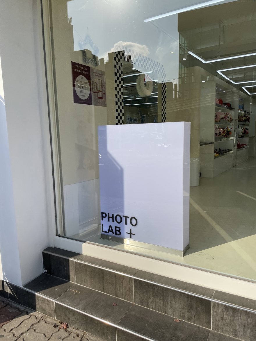 PHOTO LAB+ 門市外觀，白色招牌與整片玻璃立面，門口有階梯