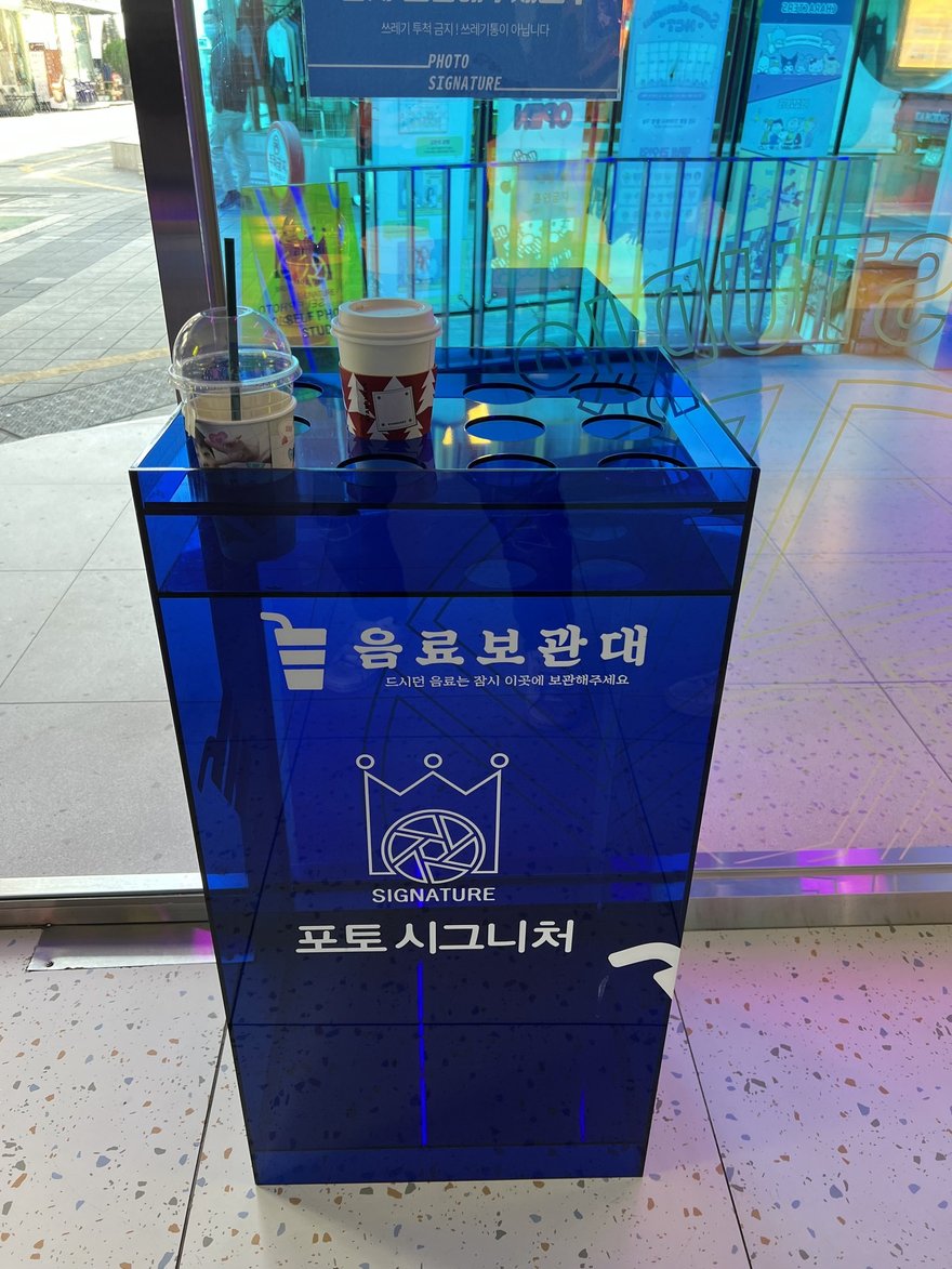 Photo Signature 門口的藍色壓克力雨傘保管架，箱體印有포토 시그니처品牌名與우산 보관대字樣