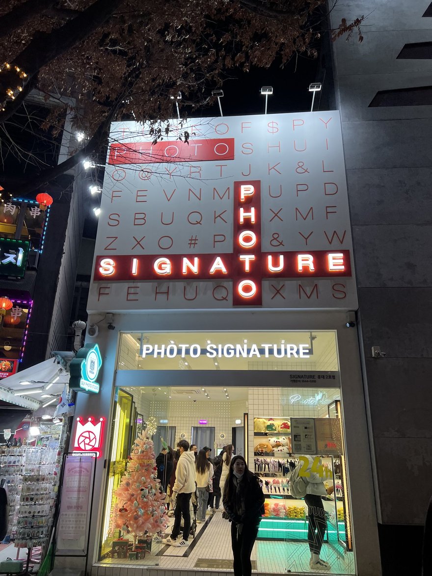 Photo Signature 街邊門市的夜間外觀，招牌燈亮著，門口有模特兒燈箱