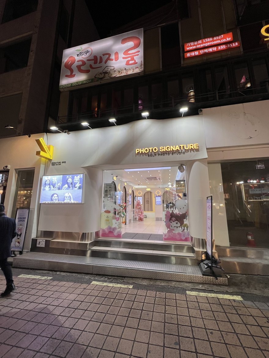 Photo Signature 夜間門市外觀，紅色 PHOTO SIGNATURE 直式招牌與騎樓入口