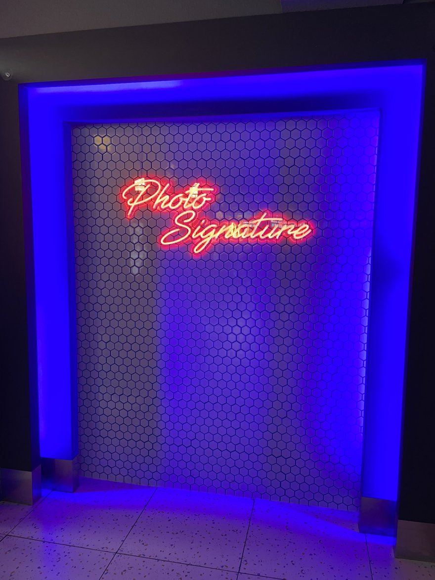 Photo Signature 的品牌霓虹燈牆，藍紫色光線襯托 Photo Signature 字樣