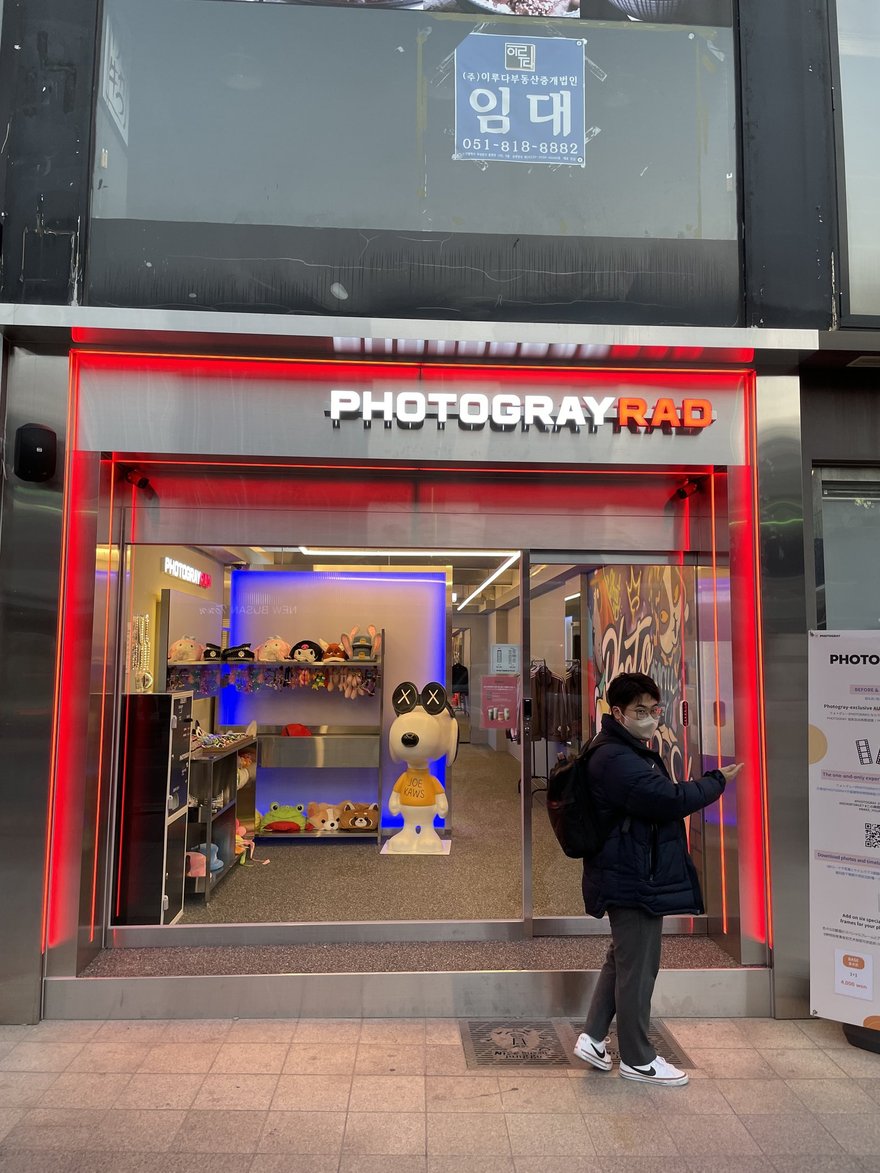 Photogray RAD 門市外觀，紅色霓虹燈框住整個店面入口，招牌寫 PHOTOGRAY RAD，店內可見道具架與大型玩偶立牌