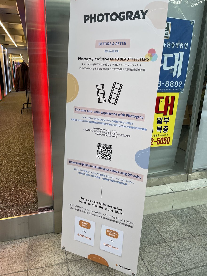 Photogray RAD 門口的四語立式看板，以韓文、日文、繁體中文與英文並列四項賣點，底部標示 BASE 1+1 四千韓元與 SPECIAL 1+1 五千韓元