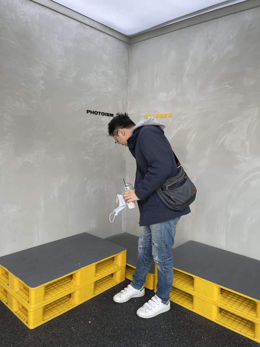 PHOTOISM COLORED 的拍攝棚，水泥質感牆面搭配 PHOTOISM 標示與黃色塑膠棧板座位