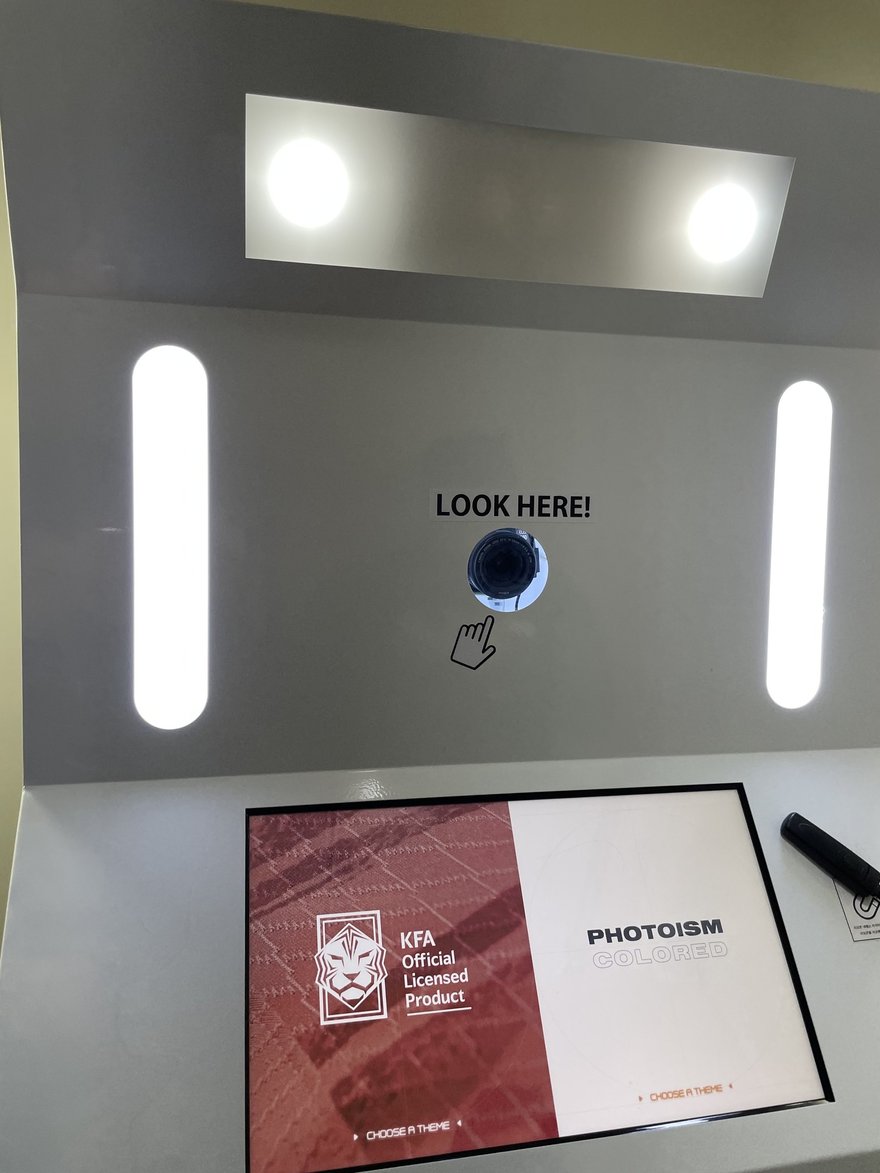 PHOTOISM COLORED 的機台上方 LOOK HERE 指示與圓形鏡頭，下方為橫式觸控螢幕