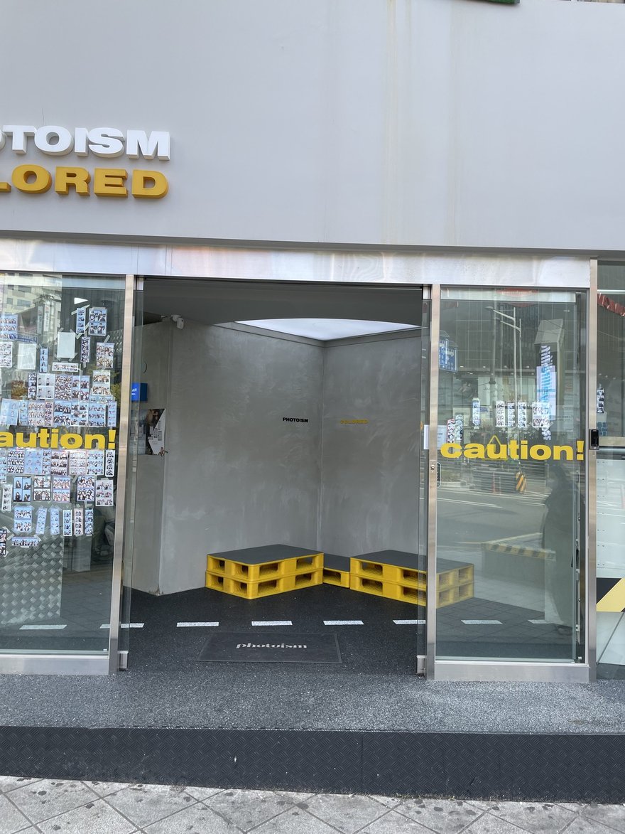PHOTOISM COLORED 門市入口特寫，招牌與 caution 標示同框