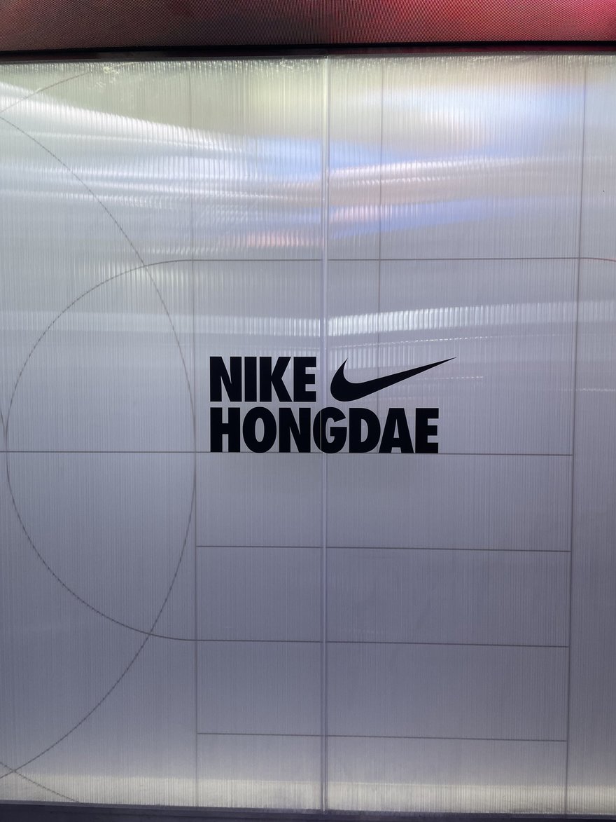 Photomatic 拍照亭內的拍攝背景牆，灰白色牆面上印有大型 NIKE 標誌與 NIKE HONGDAE 字樣