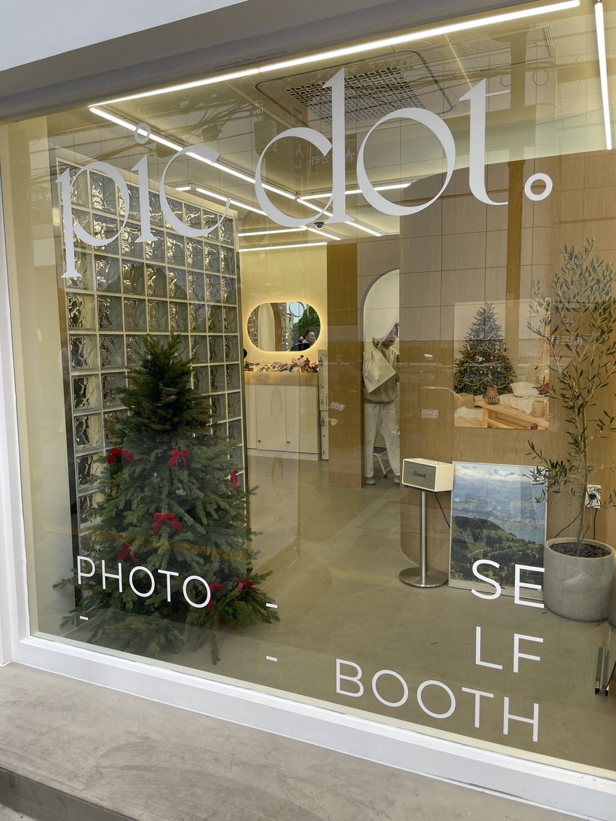 pic dot 店面的玻璃磚立面與櫥窗，玻璃上印 PHOTO、SELF、BOOTH 字樣，室內可見圓形鏡面與聖誕樹裝飾