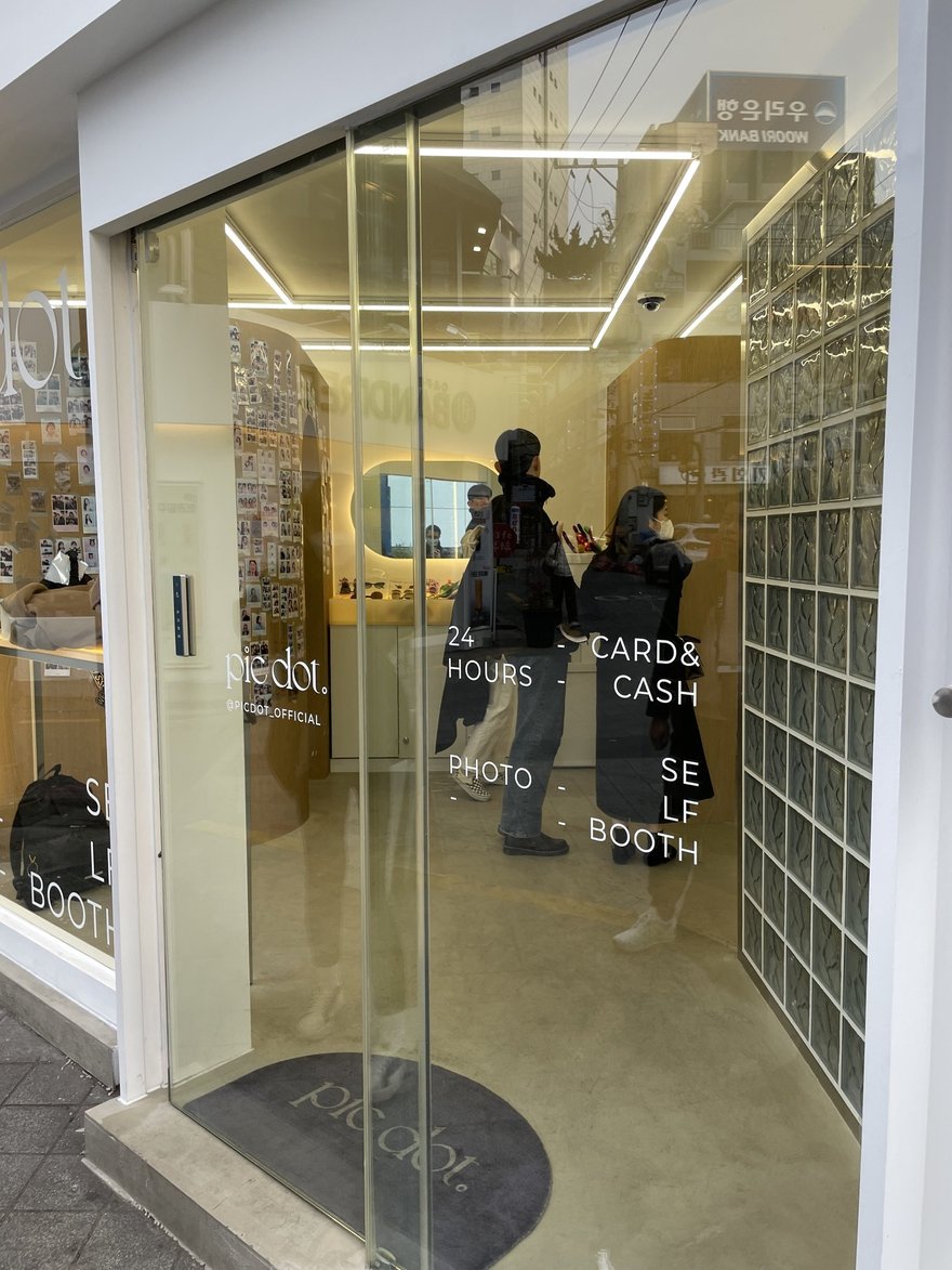 pic dot 釜山西面店的玻璃門，門上以白色字體分兩欄刻著 24 HOURS、CARD & CASH、PHOTO、SELF BOOTH，左下角印品牌名 pic dot 與 Instagram 帳號 PICDOT OFFICIAL