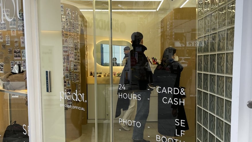 pic dot 釜山西面店的玻璃門，門上以白字刻著 24 HOURS、CARD & CASH、PHOTO SELF BOOTH，左側印品牌名 pic dot，店內可見樣張牆與圓形鏡子。