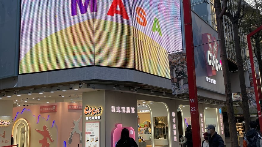 西門町 MASA 大樓轉角，巨型弧形 LED 幕牆正下方一整排店面掛著 Cut Cut+ 韓式寫真館招牌，柱面價目燈箱標示單場 200 元，左側立牌寫「請上 2F」。