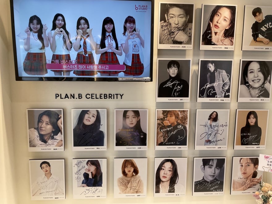 Plan.B Studio 西門店的 PLAN.B CELEBRITY 韓星簽名牆，貼滿韓國藝人簽名拍立得，上方電視循環播放韓國女團 Busters 的代言影片