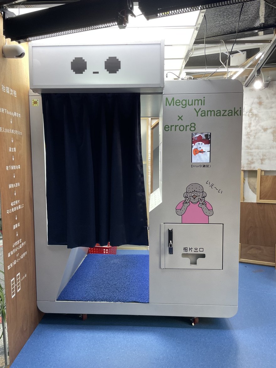 Error8 鼬鼠台北太原路店的拍貼機正面近拍，機台側面印著 Megumi Yamazaki × error8 的聯名字樣與小螢幕樣張，出片口標示相片出口，左側木板是完整的拍攝流程與價目告示