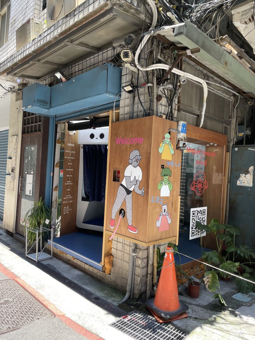 Error8 鼬鼠台北太原路店的木作門面，門口擺三角錐與盆栽，機台頂端是像素風格的表情燈箱，右側木牆寫著 Welcome 並畫著日本插畫家的角色
