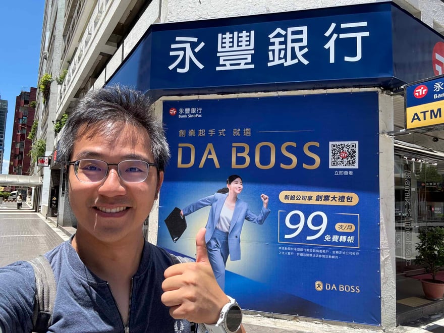 老喬在永豐銀行分行門口自拍，背後是 2025 年 DA BOSS「創業起手式」看板，主打新設公司享創業大禮包、每月 99 次免費轉帳
