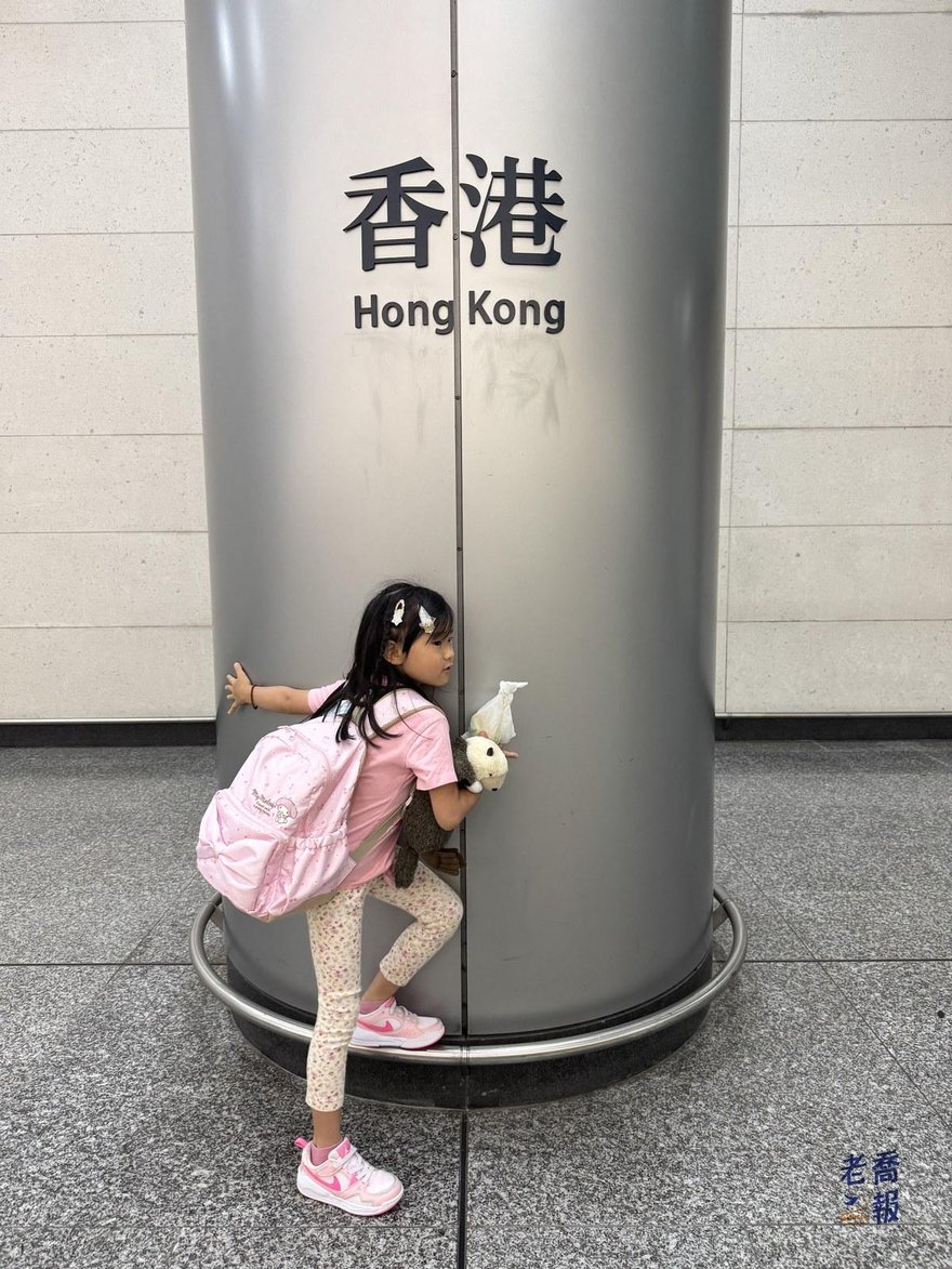 香港站月台旁寫著香港 Hong Kong 的大型圓柱，哈哈站在柱子邊