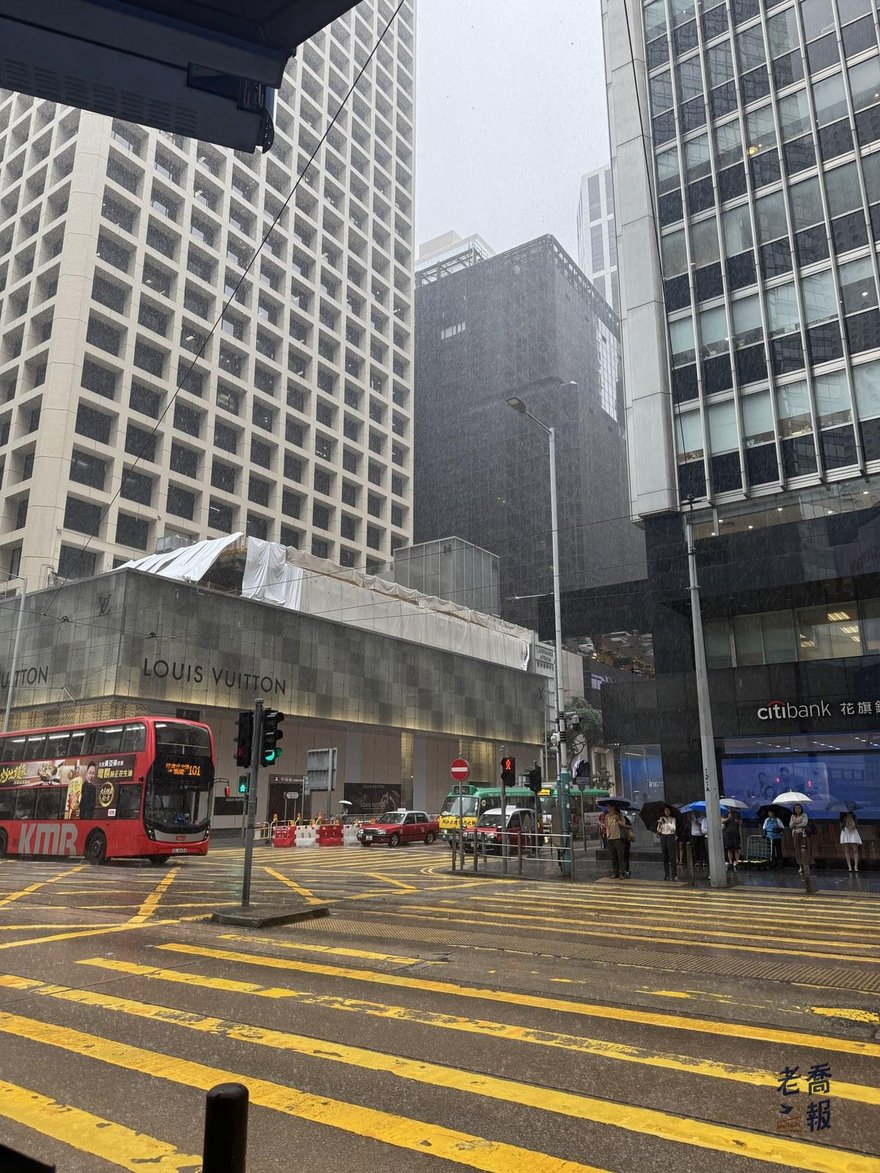 雨天的中環街景，馬路上的黃色斑馬線與雙層巴士，背景是商業大樓