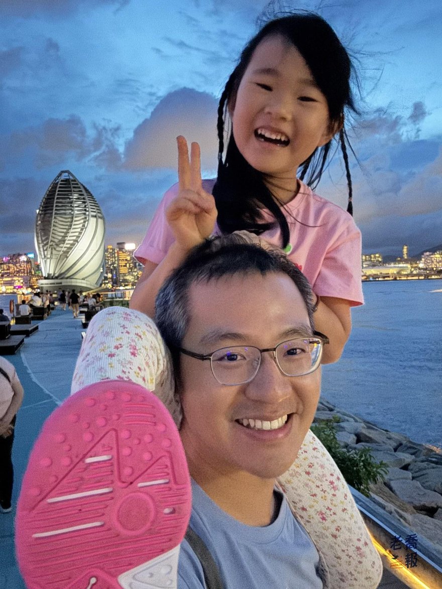 老喬與哈哈在海濱的蛋形裝置藝術旁自拍，背景是維港夜景