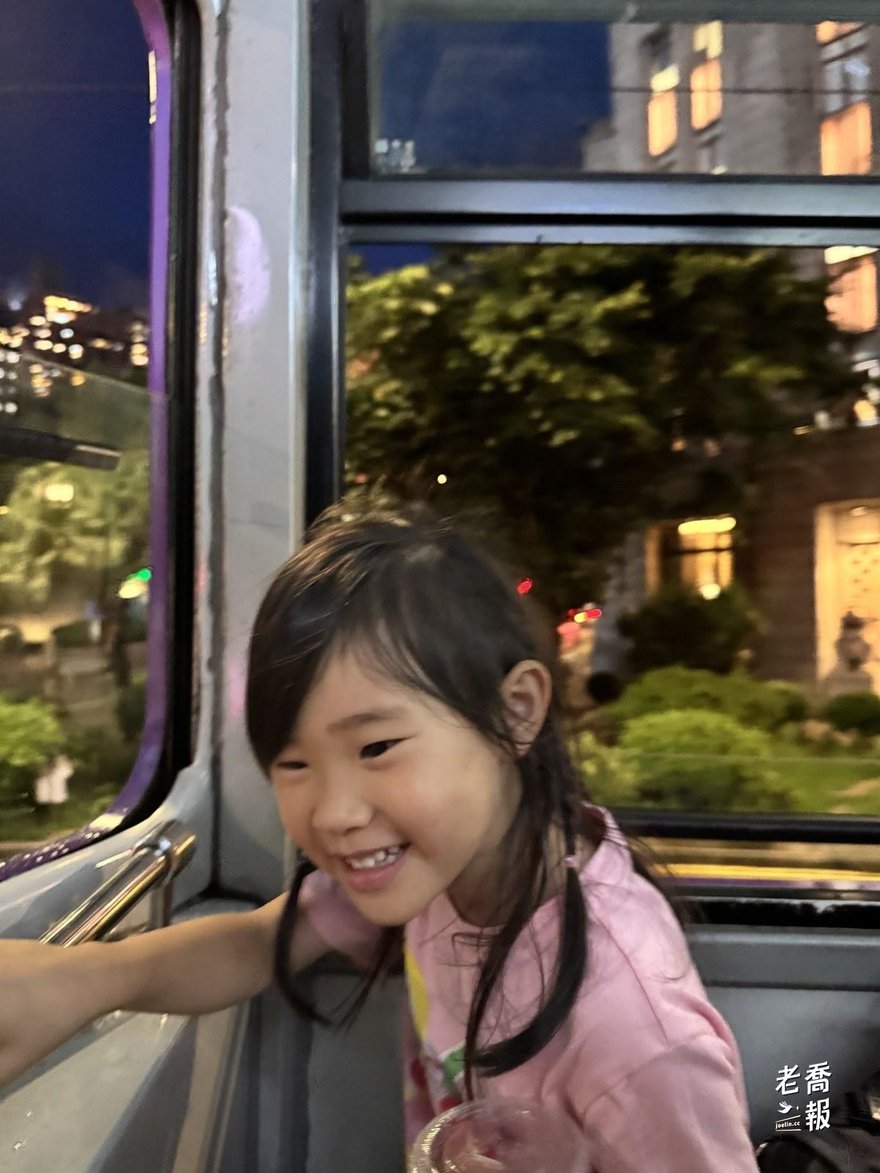 從叮叮車窗戶看出去的夜間街景，兩旁是亮著燈的店家
