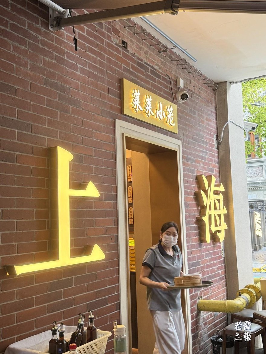 萊萊小籠店門口，木質招牌寫著萊萊小籠，門邊是發光的上海二字霓虹，店員端著蒸籠走出來