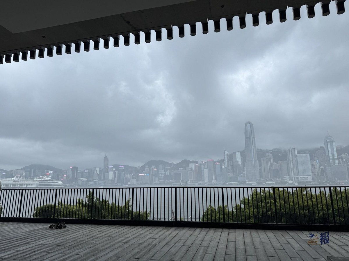 從 M+ 戶外平台看出去的維多利亞港，陰天下的港島高樓與前方的草地步道