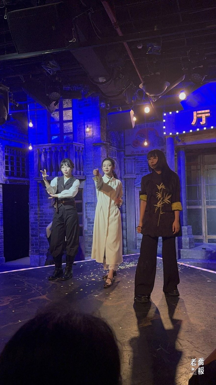 破牆返場開始，三位女演員站在藍色燈光的民國街景布景前，左邊是穿白襯衫黑背心的沈亮，中間是穿米白色長風衣的薛臨，右邊是穿深色改良旗袍的小月，地上散著黃色花瓣