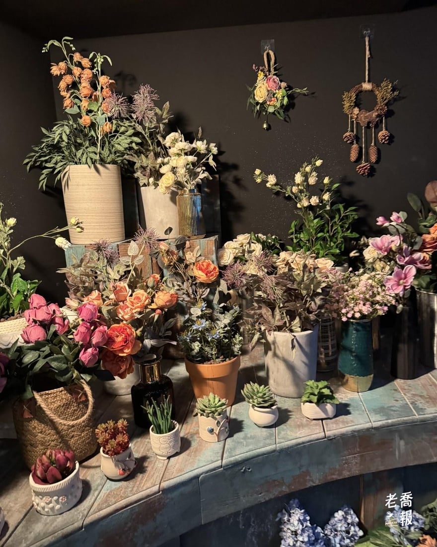 白爪草的花店實景舞台，牆邊排滿各式盆栽、乾燥花與花器，牆上掛著花圈與小花束