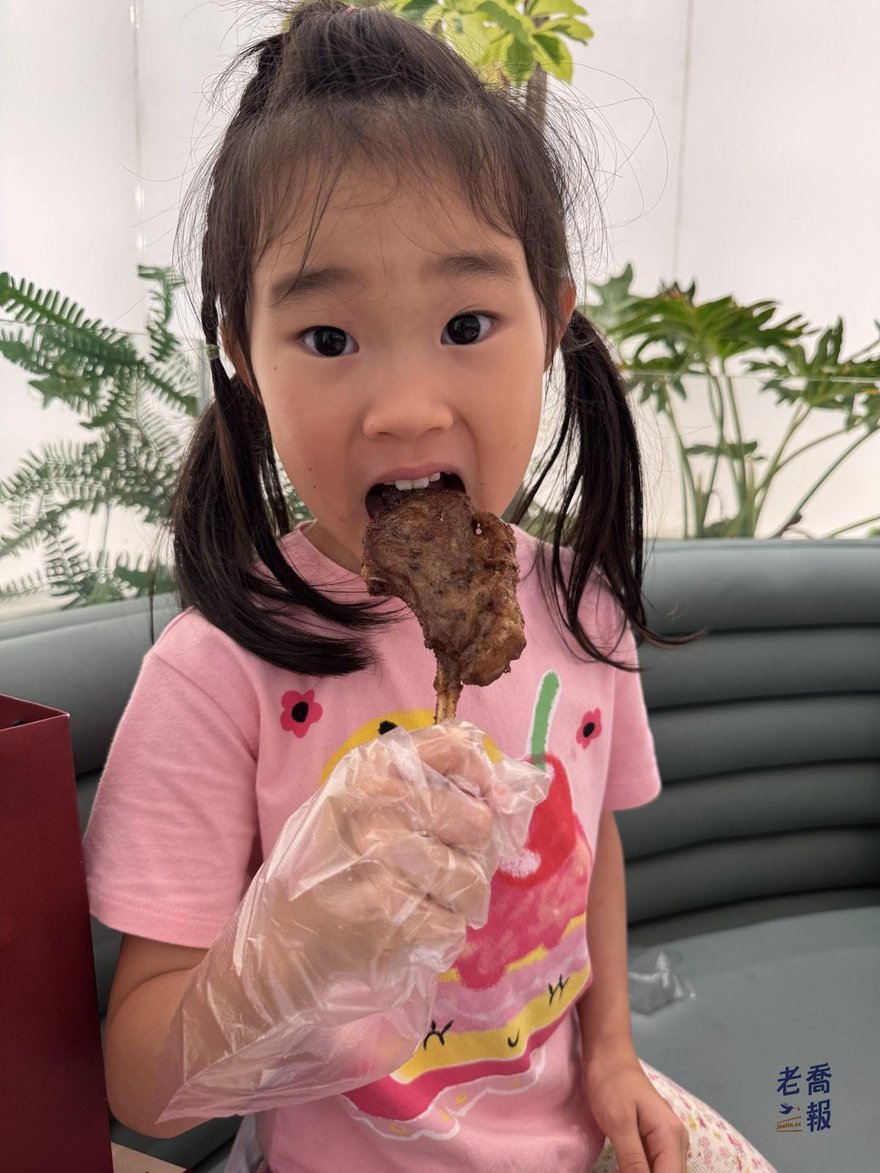 哈哈戴著透明塑膠手套，雙手捧著一支帶骨羊排在吃，背景是店內綠植