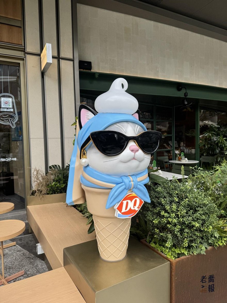 西岸中環二期店門口的 DQ 冰淇淋造型公仔，戴著墨鏡與藍色頭巾，旁邊是綠色植栽與戶外座位