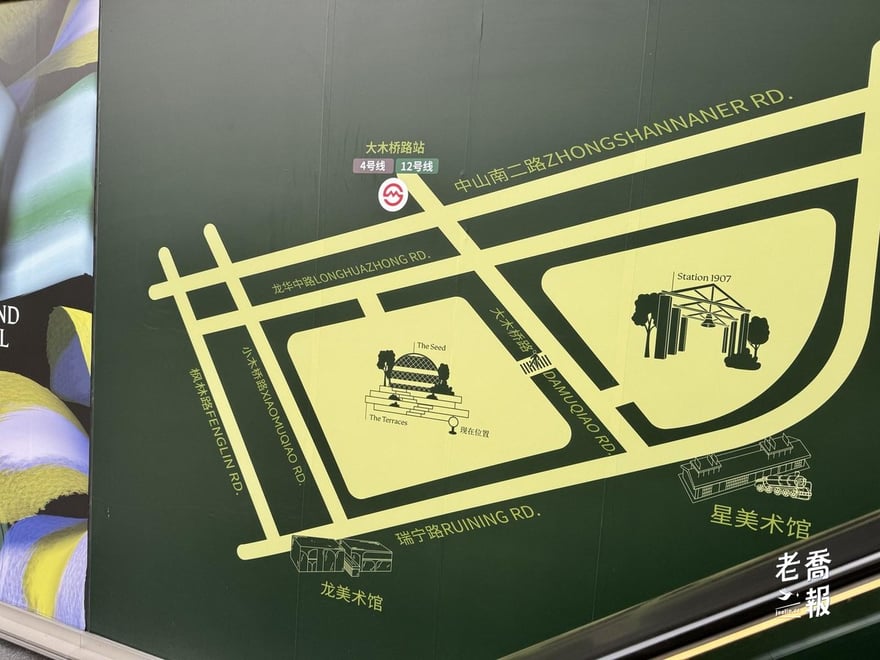 西岸中環二期工地圍擋上的黃綠色區域地圖，標出大木橋路站 4 號線與 12 號線、中山南二路、龍華中路、瑞寧路、大木橋路，以及 The Seed 種子館、The Terraces 梯田、龍美術館、星美術館與 Station 1907，並有「現在位置」標記