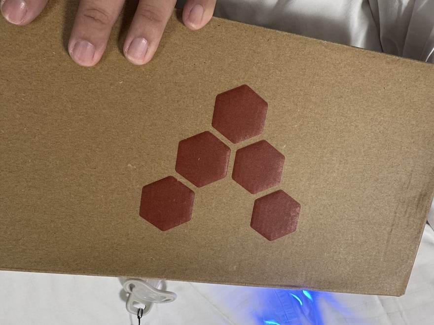 Vivobarefoot 鞋盒側面印著品牌的六邊形蜂巢標誌，五個紅褐色六邊形排列在牛皮紙色的盒身上。