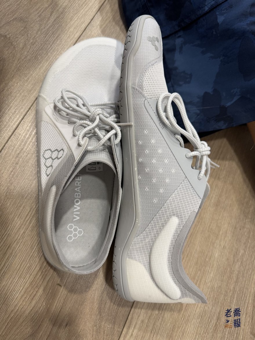 Vivobarefoot Primus Lite IV 實鞋側面：一隻鞋側立、一隻鞋平放，可以看出鞋底完全水平沒有後跟墊高，鞋底厚度極薄，鞋身為礦石灰網布並在側面印有品牌六邊形標誌。