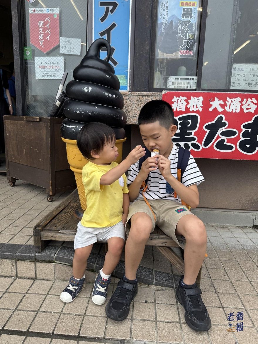 圈圈與嘻嘻坐在黑霜淇淋模型前，圈圈用手抓著嘴邊的東西，嘻嘻正在咬霜淇淋