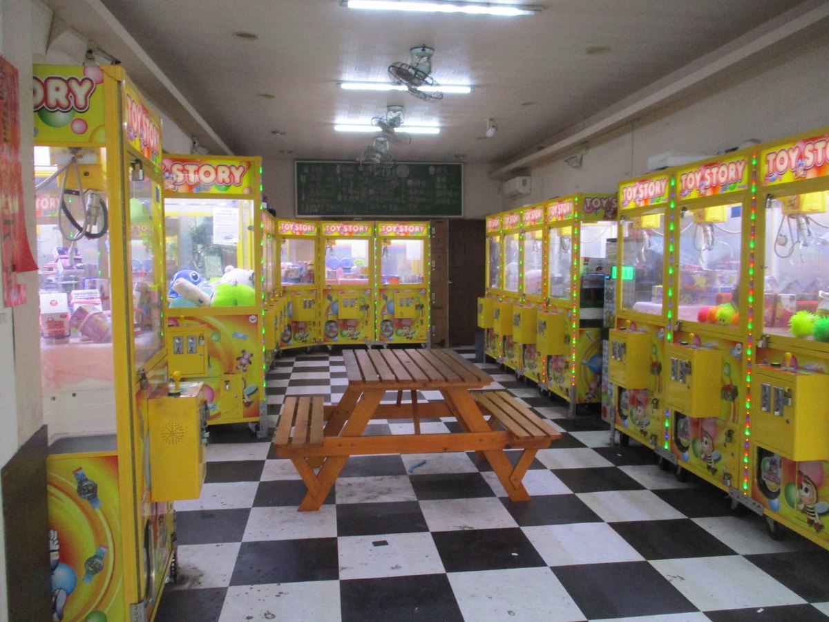 新竹市水田街的一間夾娃娃機店，左右兩排黃色機台，中間擺著一張木製野餐桌，地板是黑白格磁磚，店內沒有人，2020 年 8 月拍攝。
